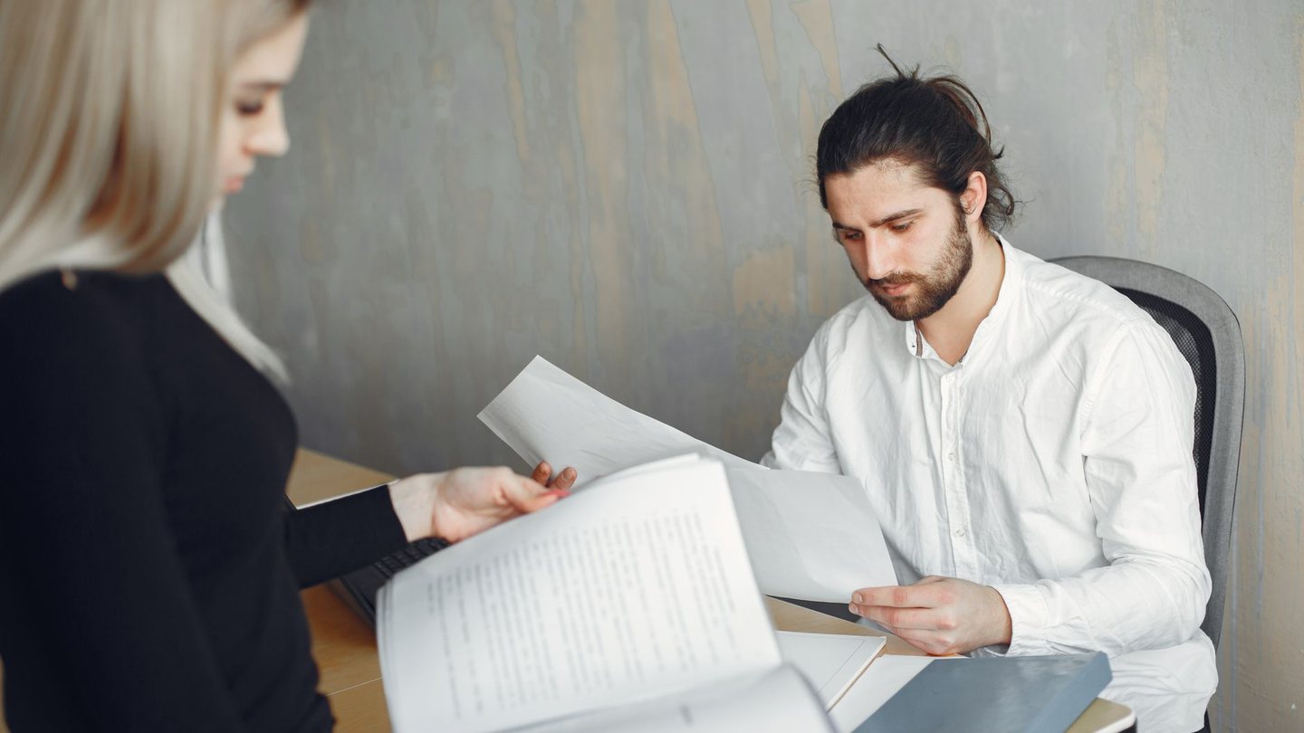 Two colleagues at a desk working through a bound document and a loose page side by side